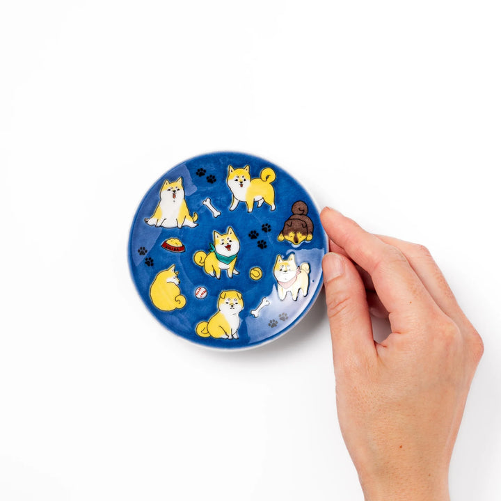 Round Japanese ceramic sauce dish with a deep blue background decorated with playful Shiba Inu dogs, paw prints, and bones, perfect for condiments or snacks.
