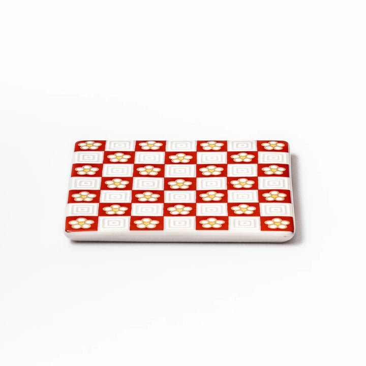 Square Japanese ceramic coaster with red and white checkered pattern decorated with plum blossom motifs, adding traditional charm to any dining table.