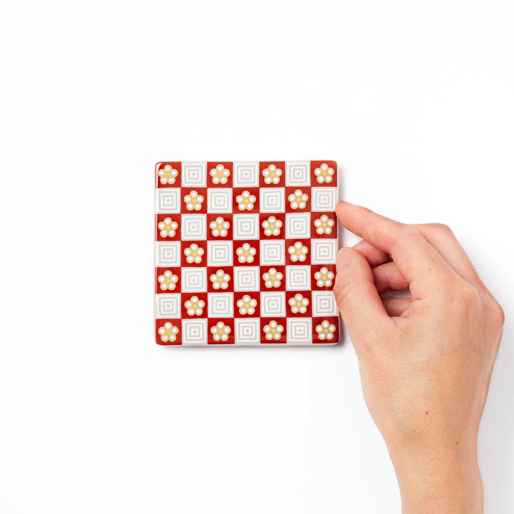 Square Japanese ceramic coaster with red and white checkered pattern decorated with plum blossom motifs, adding traditional charm to any dining table.