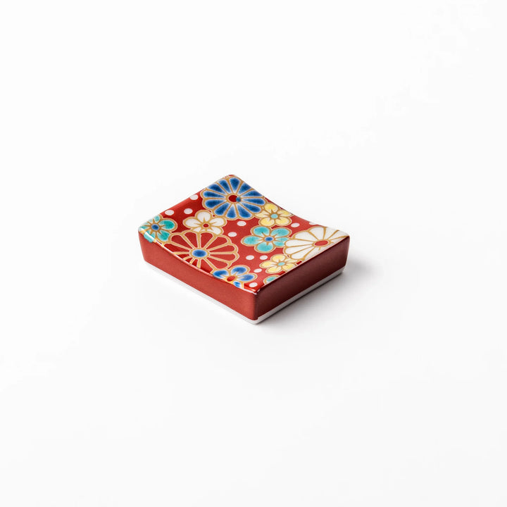 Rectangular Japanese ceramic chopstick rest with a red background decorated with colorful plum and chrysanthemum blossoms, perfect for elegant dining settings.