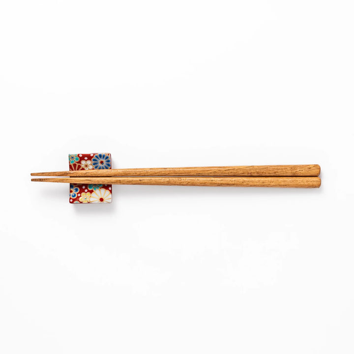 Rectangular Japanese ceramic chopstick rest with a red background decorated with colorful plum and chrysanthemum blossoms, perfect for elegant dining settings.