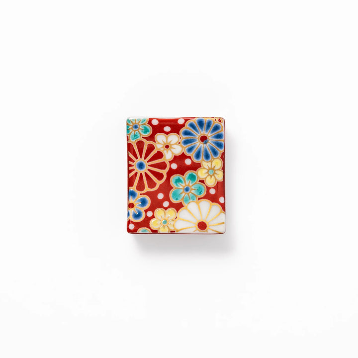 Rectangular Japanese ceramic chopstick rest with a red background decorated with colorful plum and chrysanthemum blossoms, perfect for elegant dining settings.
