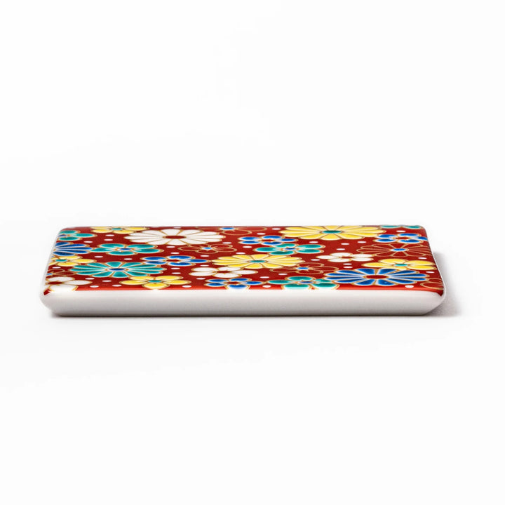 Square Japanese ceramic coaster with a red background decorated with colorful plum and chrysanthemum blossoms, adding elegance and tradition to table settings.