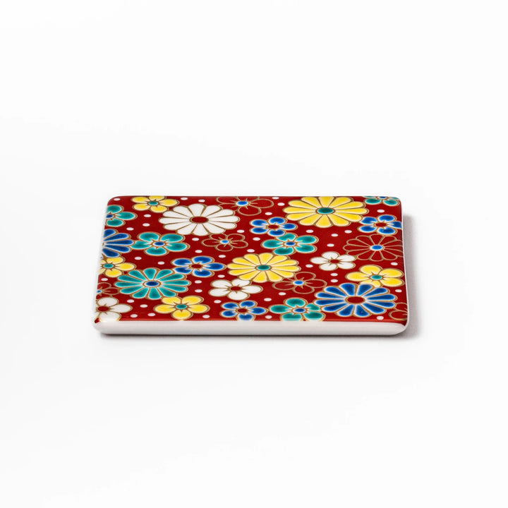 Square Japanese ceramic coaster with a red background decorated with colorful plum and chrysanthemum blossoms, adding elegance and tradition to table settings.