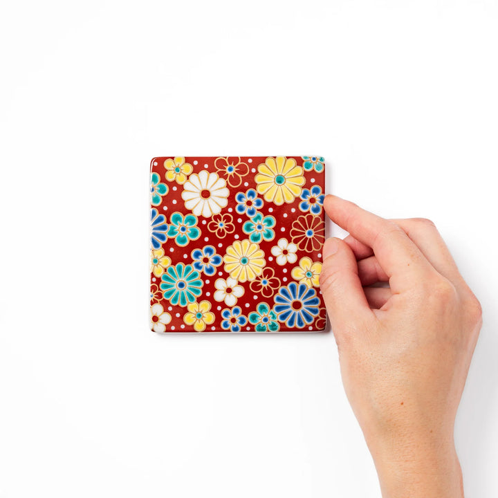 Square Japanese ceramic coaster with a red background decorated with colorful plum and chrysanthemum blossoms, adding elegance and tradition to table settings.