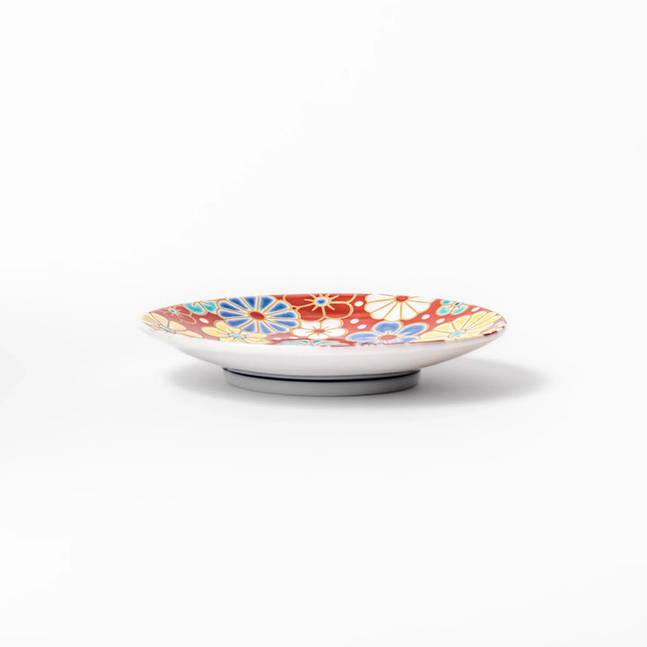Round Japanese ceramic sauce dish with a red background decorated with colorful plum and chrysanthemum blossoms, perfect for serving soy sauce or condiments.