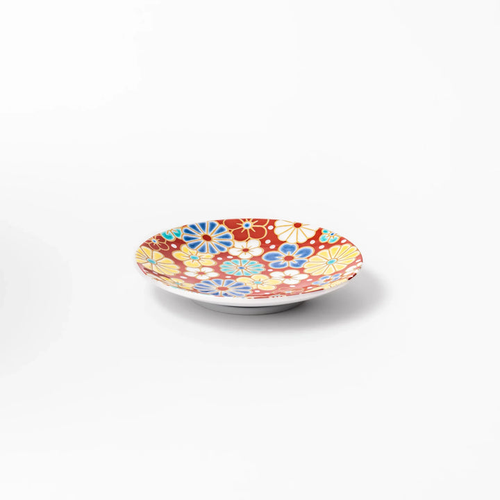 Round Japanese ceramic sauce dish with a red background decorated with colorful plum and chrysanthemum blossoms, perfect for serving soy sauce or condiments.