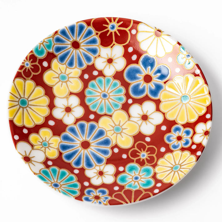 Round Japanese ceramic sauce dish with a red background decorated with colorful plum and chrysanthemum blossoms, perfect for serving soy sauce or condiments.