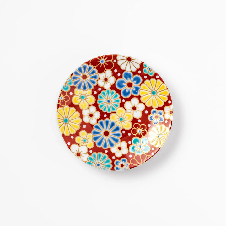 Round Japanese ceramic sauce dish with a red background decorated with colorful plum and chrysanthemum blossoms, perfect for serving soy sauce or condiments.