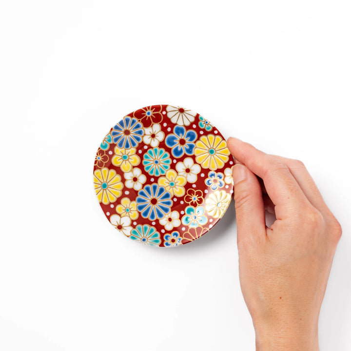 Round Japanese ceramic sauce dish with a red background decorated with colorful plum and chrysanthemum blossoms, perfect for serving soy sauce or condiments.