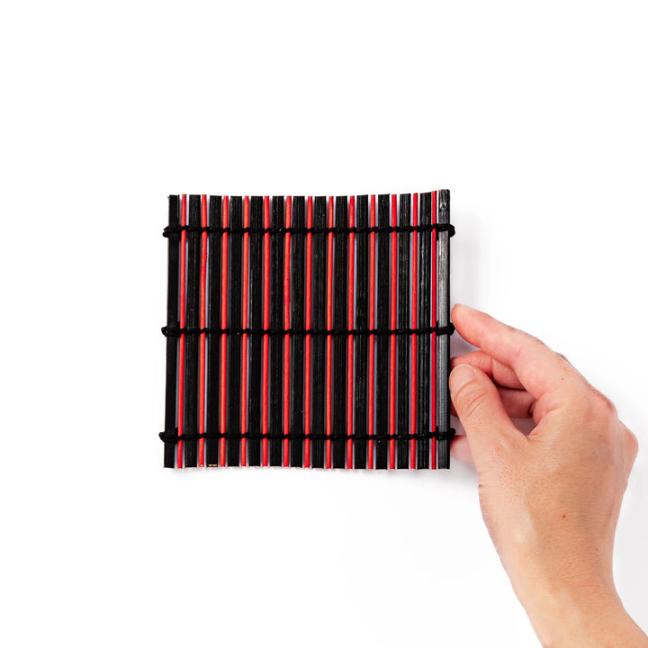 Red and black bamboo coaster with slim vertical slats and black cord ties, ideal for adding a striking accent to Japanese-style drink settings.