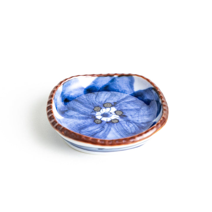 A round plate featuring a large, bold blue flower with a textured brown rim.