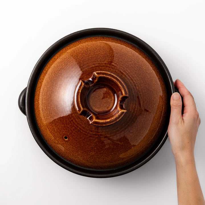 Japanese donabe clay pot with rustic brown glazed lid and black base, induction compatible and perfect for family hot pot meals.