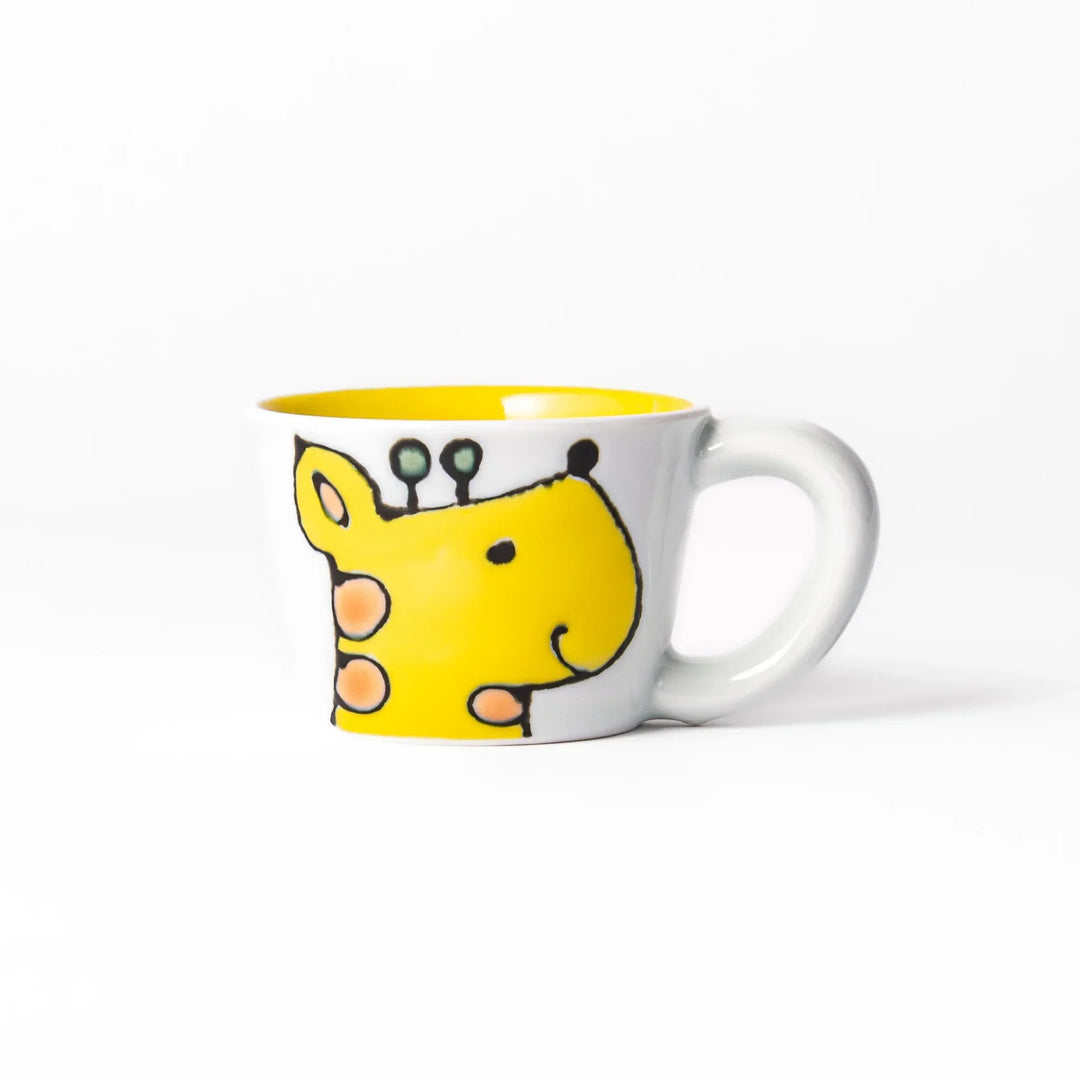 White ceramic kids mug featuring smiling yellow giraffe with green ossicones, vibrant yellow interior, round handle, shown on white background