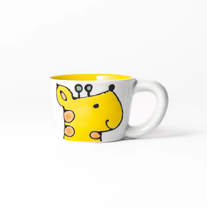 White ceramic kids mug featuring smiling yellow giraffe with green ossicones, vibrant yellow interior, round handle, shown on white background