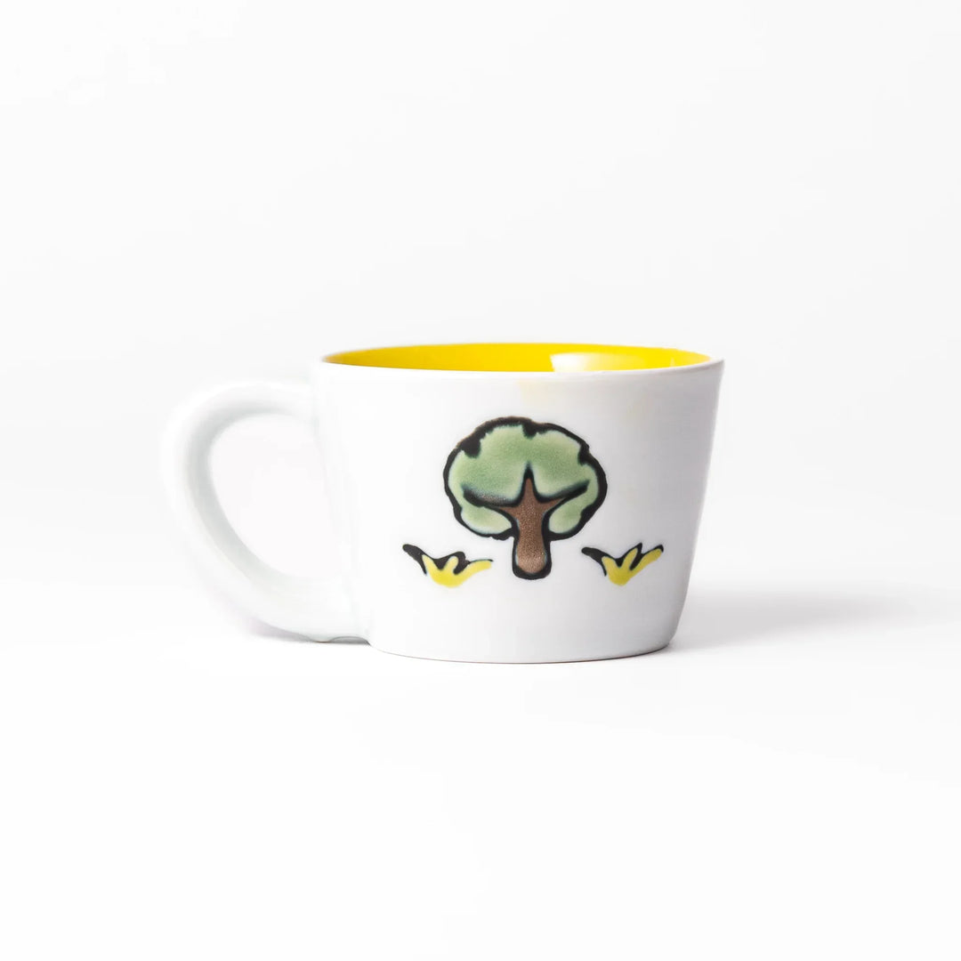 White ceramic kids mug featuring smiling yellow giraffe with green ossicones, vibrant yellow interior, round handle, shown on white background