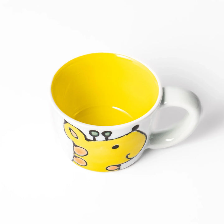 White ceramic kids mug featuring smiling yellow giraffe with green ossicones, vibrant yellow interior, round handle, shown on white background