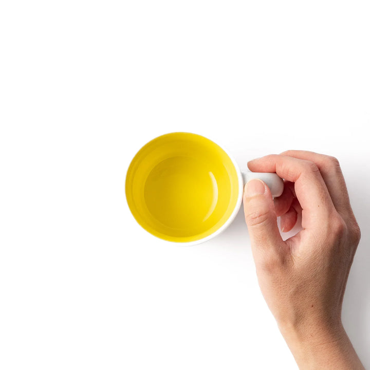 White ceramic kids mug featuring smiling yellow giraffe with green ossicones, vibrant yellow interior, round handle, shown on white background