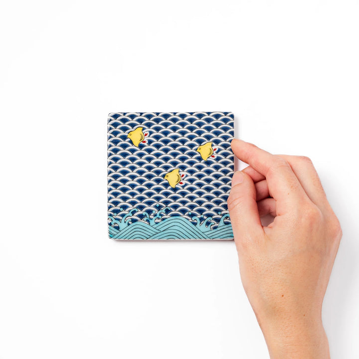Square Japanese ceramic coaster with traditional blue wave pattern and yellow shorebirds, combining artistry and function for stylish dining table settings.