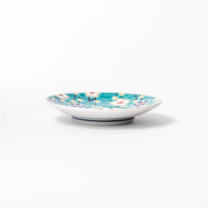 Round Japanese ceramic sauce dish with teal background, decorated with white and blue plum blossom motifs, perfect for serving condiments or small bites.