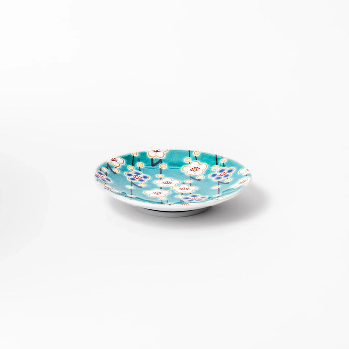 Round Japanese ceramic sauce dish with teal background, decorated with white and blue plum blossom motifs, perfect for serving condiments or small bites.