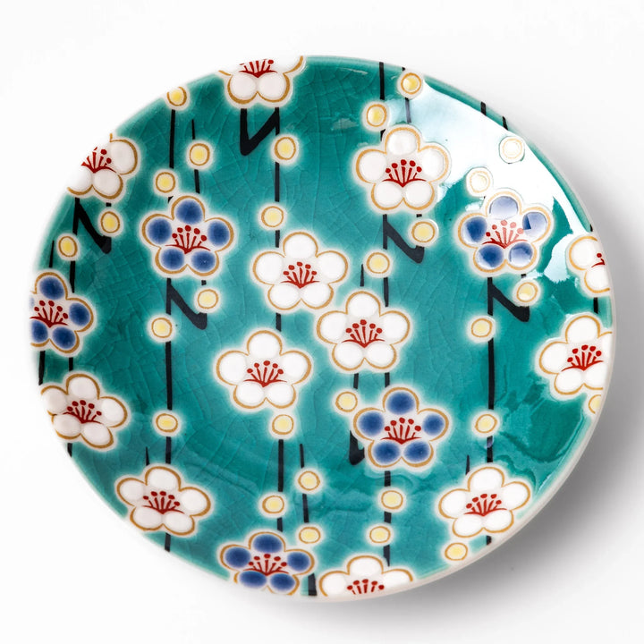 Round Japanese ceramic sauce dish with teal background, decorated with white and blue plum blossom motifs, perfect for serving condiments or small bites.