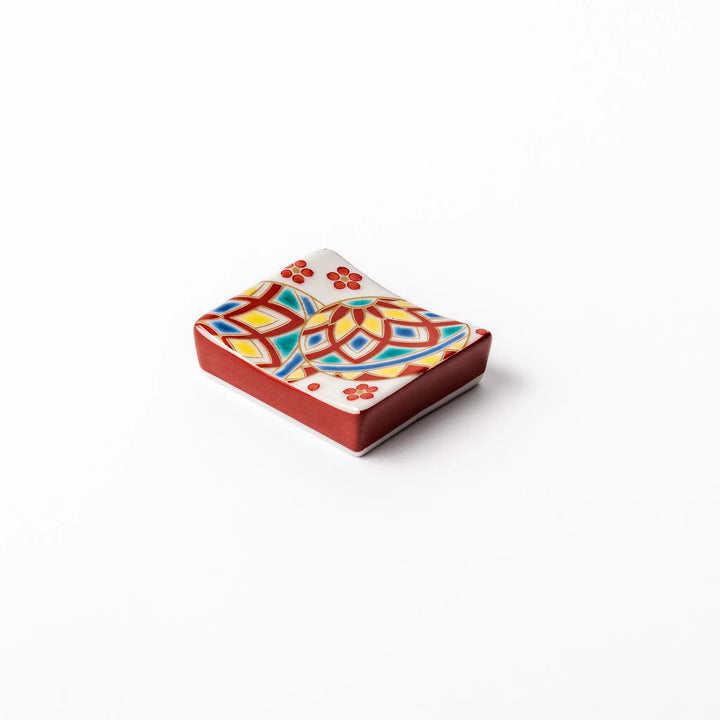 Rectangular Japanese ceramic chopstick rest adorned with colorful temari ball patterns and red floral accents, bringing vibrant charm to any dining table.