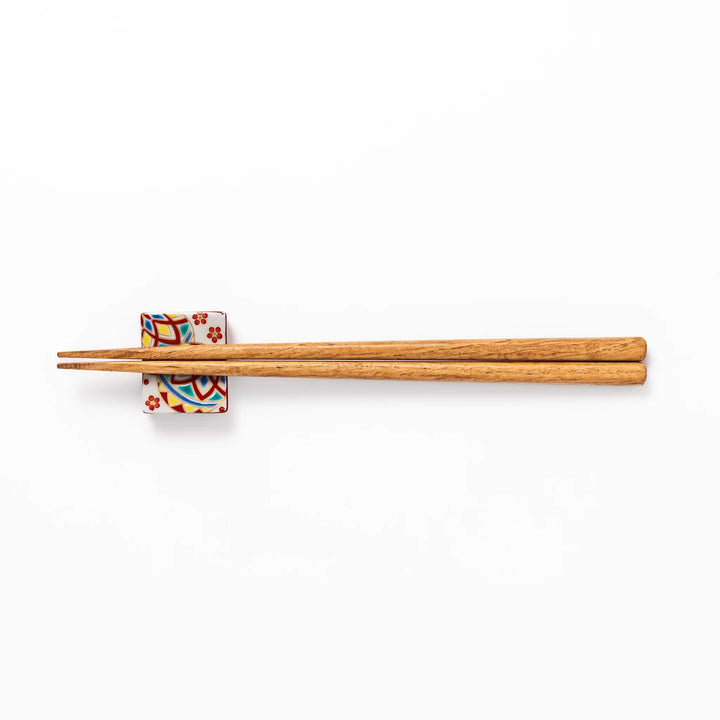 Rectangular Japanese ceramic chopstick rest adorned with colorful temari ball patterns and red floral accents, bringing vibrant charm to any dining table.