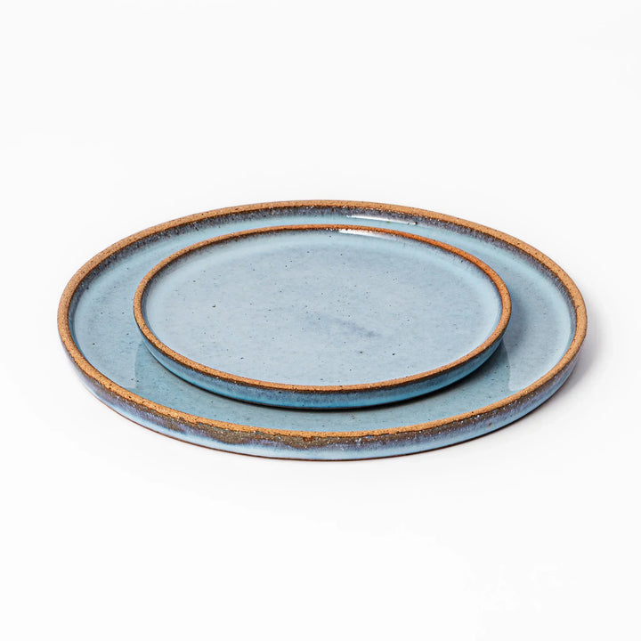 Terracotta blue ceramic plates in two different sizes with rustic brown rims, handcrafted in Japan and stacked for versatile table setting.