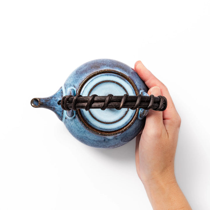 Terracotta blue ceramic teapot with rustic brown rim and woven metal handle, handcrafted in Japan for serving green tea or everyday brewing.