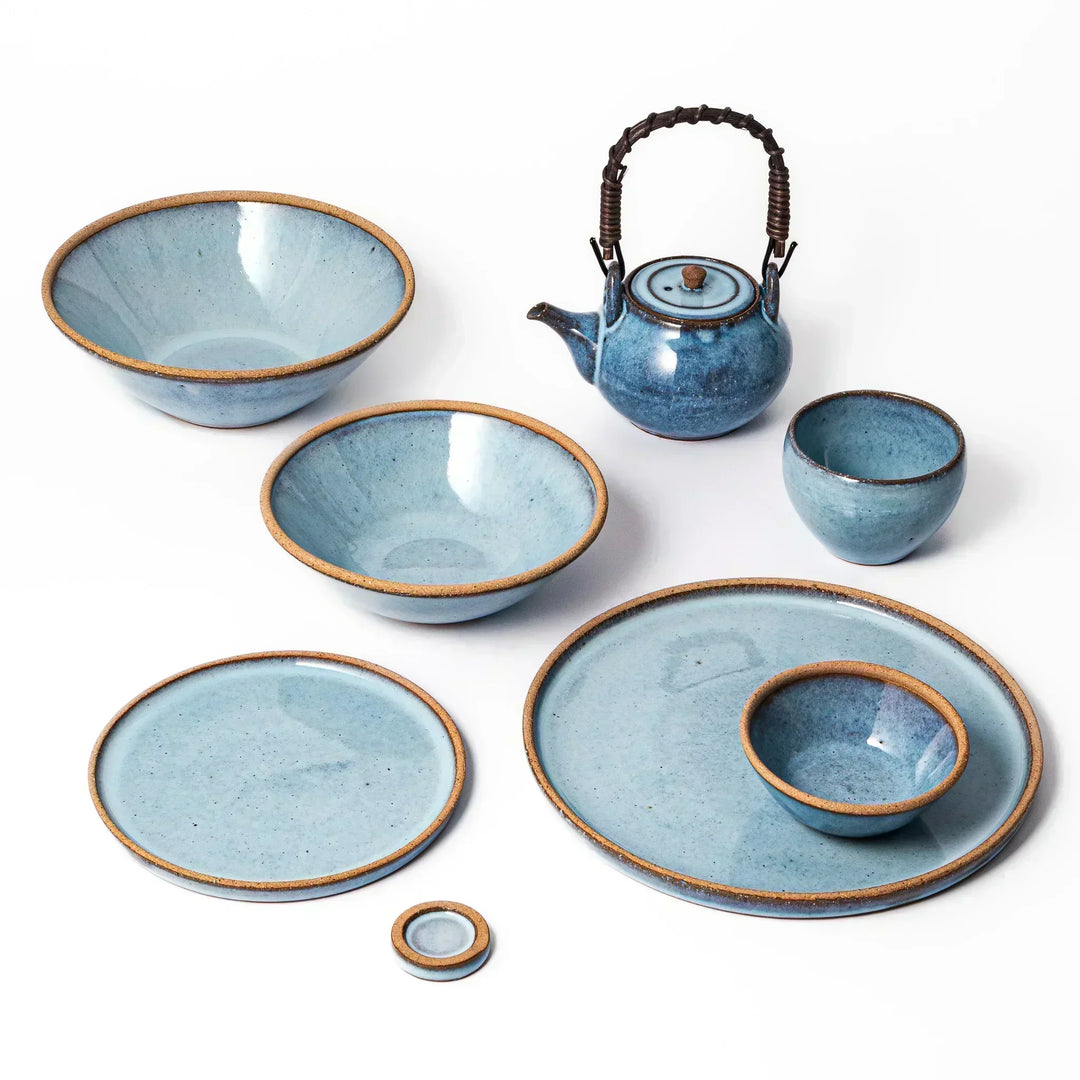 Terracotta blue Japanese ceramic tableware collection with bowls, plates, teacup, and teapot, handcrafted in Japan for everyday dining.