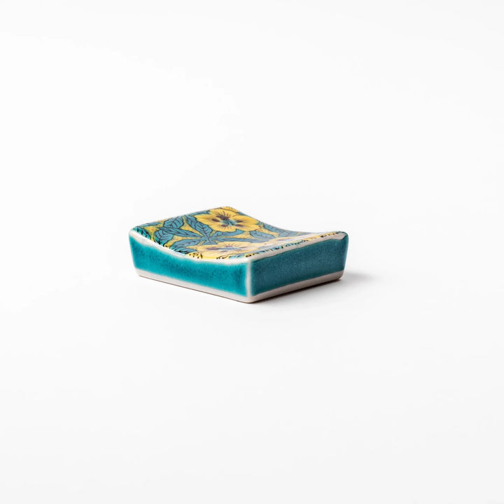 Rectangular Japanese ceramic chopstick rest decorated with vivid yellow floral design and teal leaves, bringing elegance and color to your dining table.