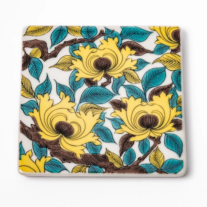 Square Japanese ceramic coaster adorned with vivid yellow peony blooms and teal leaves, adding elegance and charm to any dining table setting.