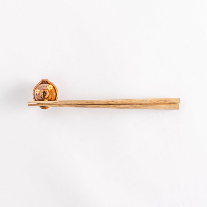 Full view of the amber earthen pot chopsticks rest with chopsticks resting horizontally.