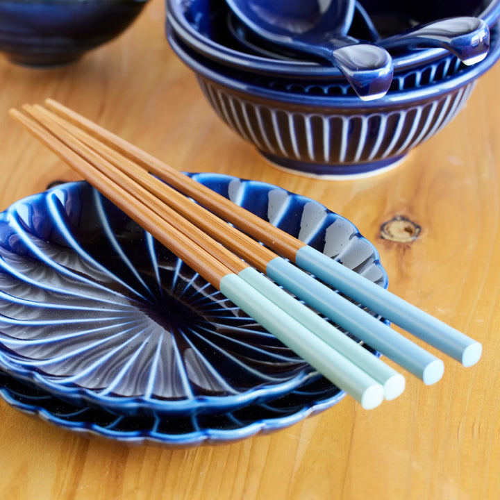 Japanese wooden chopsticks with light blue handles, resting on indigo ceramic plates, elegant utensils for everyday dining.
