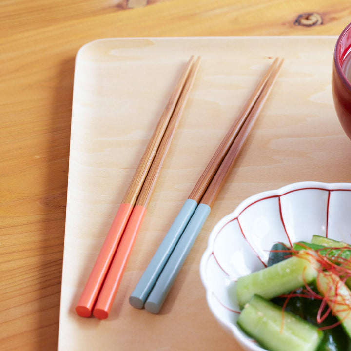Two pairs of wooden chopsticks—one with coral red handles and the other with muted blue handles.