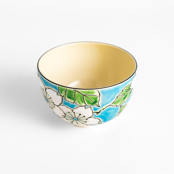 Eye-catching Matcha bowl showcasing a beautiful floral pattern in white and green against a bright blue backdrop, ideal for preparing and serving Matcha.