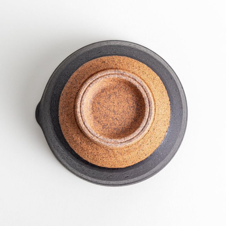 A small, black ceramic bowl with a rough texture and a natural, unglazed bottom.