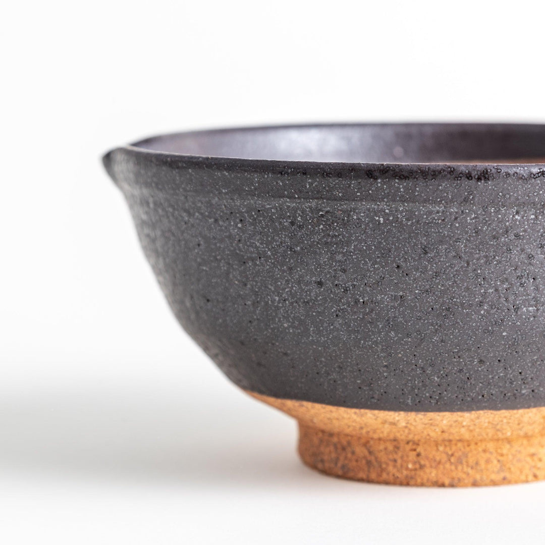 A small, black ceramic bowl with a rough texture and a natural, unglazed bottom.