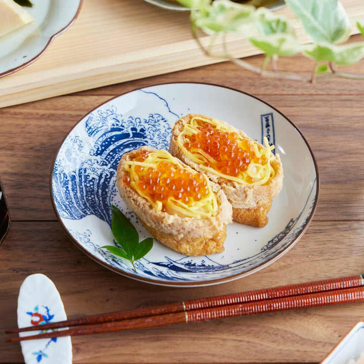 A dessert plate featuring Hokusai-style blue wave artwork, beautifully presenting two inari sushi topped with egg and salmon roe.