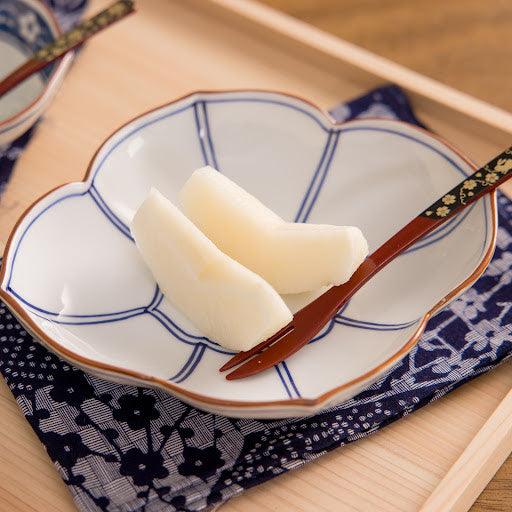 Blue-lined dessert plate with pear slices and a decorative spoon on a patterned fabric, set on a wooden tray for a refined presentation.