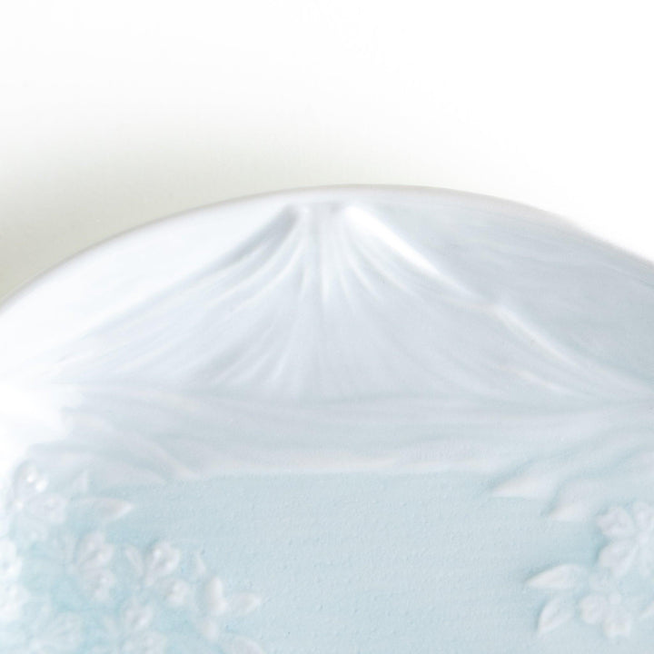 A round celadon dessert plate with a subtle raised pattern depicting Mount Fuji and surrounding nature, with a smooth, glossy finish.
