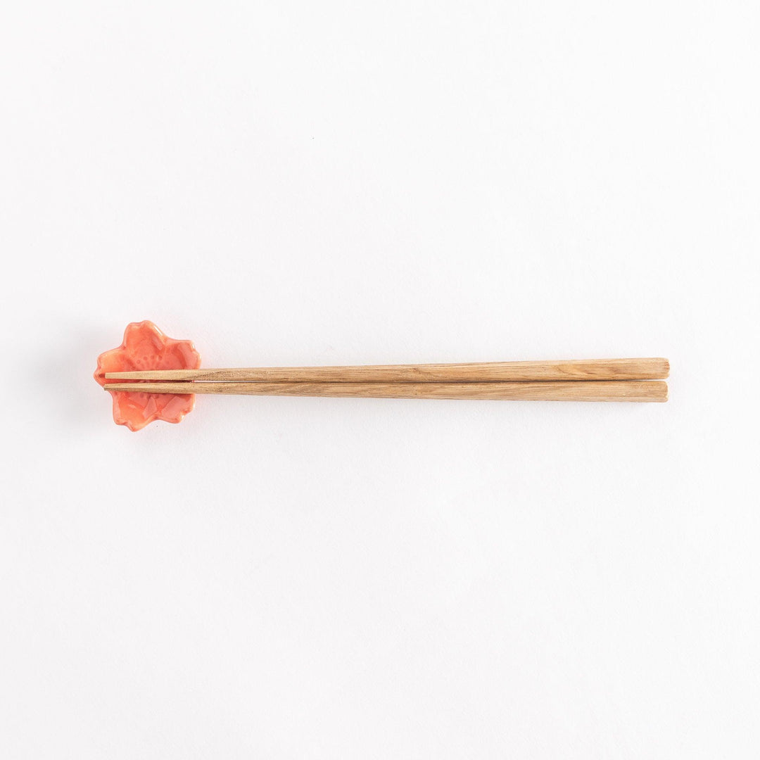 Vermilion cherry blossom chopstick rest holding chopsticks, highlighting its glossy finish and floral design.