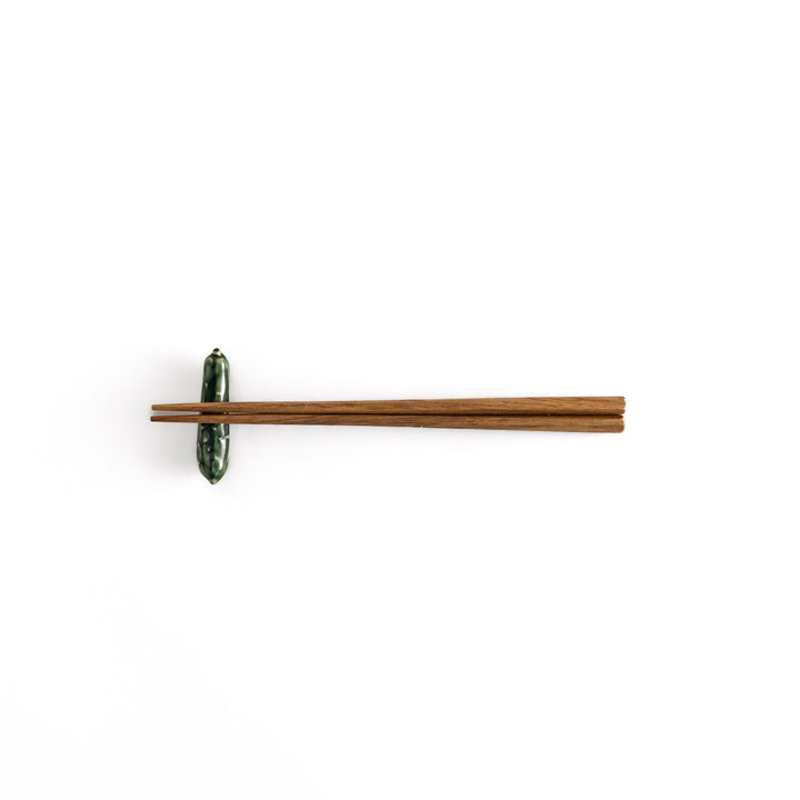 Wooden chopsticks resting on a glossy green ceramic cucumber chopstick rest, showcasing its playful design and functional elegance.