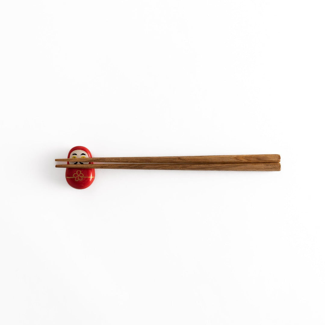 A distant view of chopsticks placed on the red daruma chopstick rest, showcasing its overall design and vibrant colors.