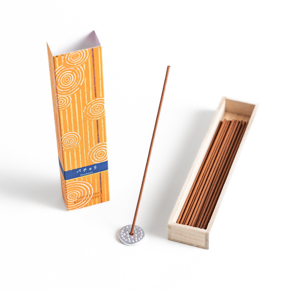 Earthy Patchouli Incense in a light wooden box with warm brown sticks, elegantly packaged in an orange design featuring white circular patterns, evoking a rich and grounding aroma.