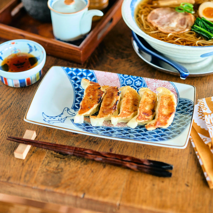 Rectangular plate with traditional Edo patterns and a blue dinosaur illustration, served with golden pan-fried gyoza on a wooden table.