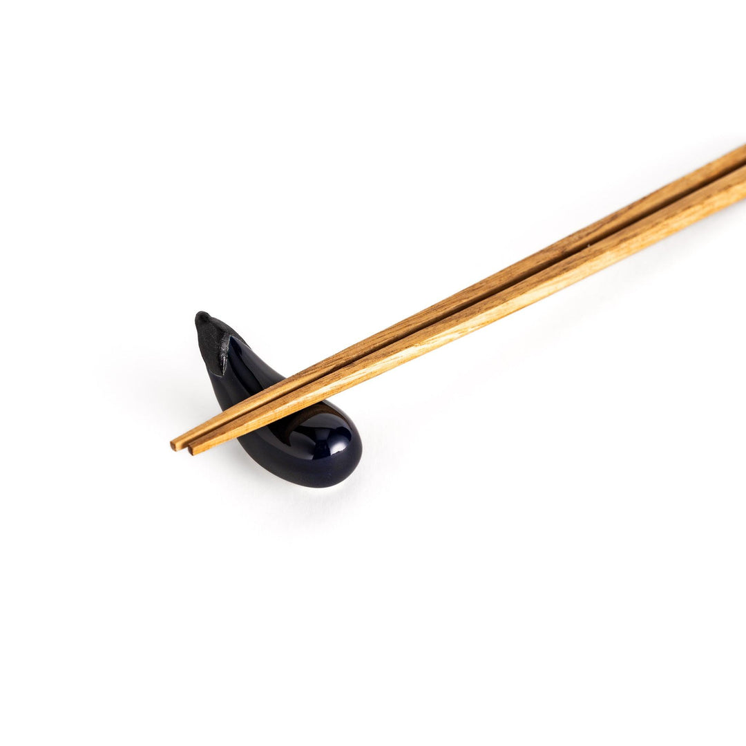 Wooden chopsticks resting on the glossy purple ceramic eggplant chopstick rest, showcasing its balance and charm.