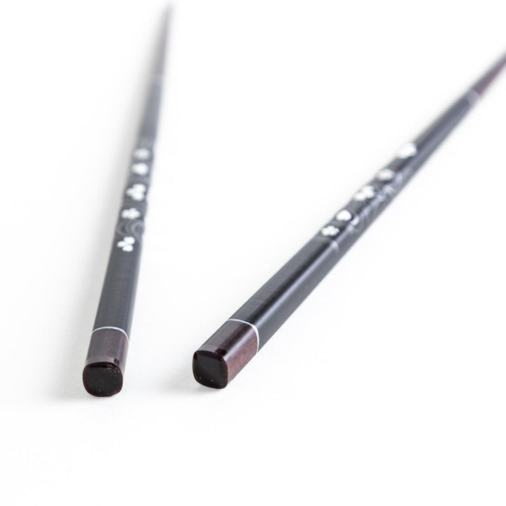 Two pairs of chopsticks, one black and one red, each adorned with intricate floral patterns on a dark background.