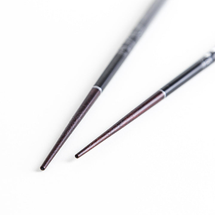 Two pairs of chopsticks, one black and one red, each adorned with intricate floral patterns on a dark background.